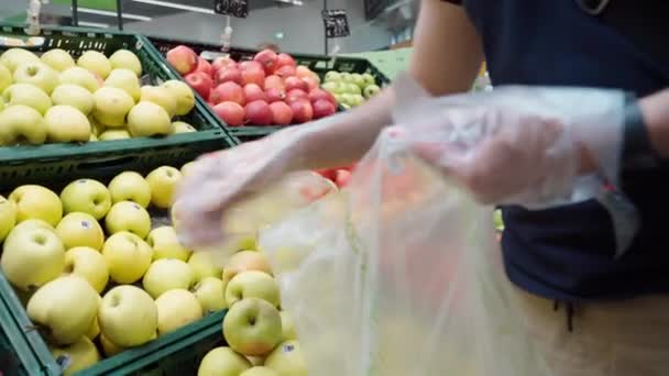 ミラノ,イタリア- 2020年5月25日:コロナウイルス発生中のスーパーマーケットでの買い物、黄色のリンゴを選んで袋に入れる保護手袋の男。免疫系を強化するための果実 — ストック動画