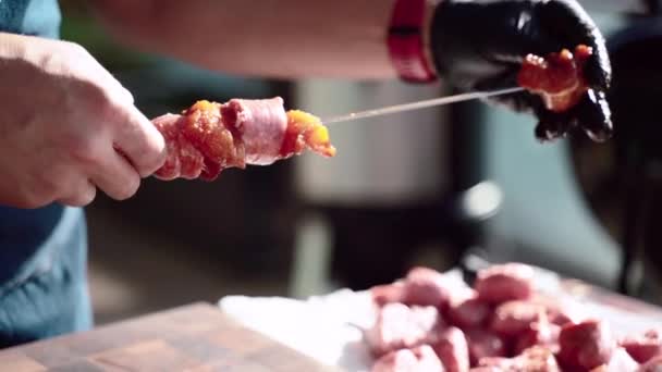 Man in het koken handschoenen stringing stukken pittige worsten en gemarineerd rundvlees vlees op metalen spiesen, de voorbereiding van rauw vlees plakken voor het roosteren op grill. Weekend cookout met assortiment van hoge kwaliteit — Stockvideo