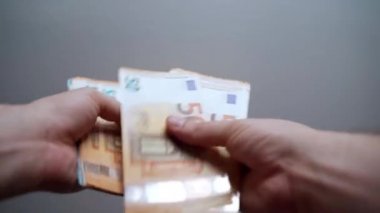 Gri arka planda kağıt para birimini hesaplayan kişiler. Adam 20 ve 50 avroluk banknotlar sayıyor, ödemeler ve diğer harcamalar için para kazanıyor. Nakit para erkeklerin elinde.