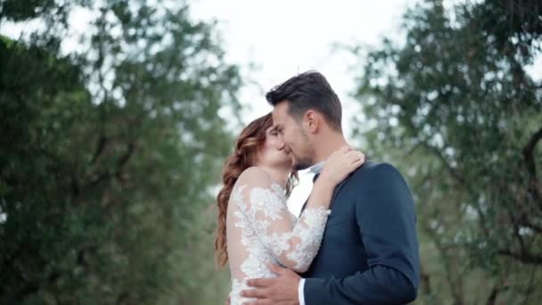 Prawdziwe emocje młodych szczęśliwych małżeństw, nowożeńców przytulających się i patrzących sobie w oczy, uśmiechniętej pary cieszącej się sobą w pięknym zielonym ogrodzie. Pasja i miłość między mężczyzną a kobietą — Wideo stockowe