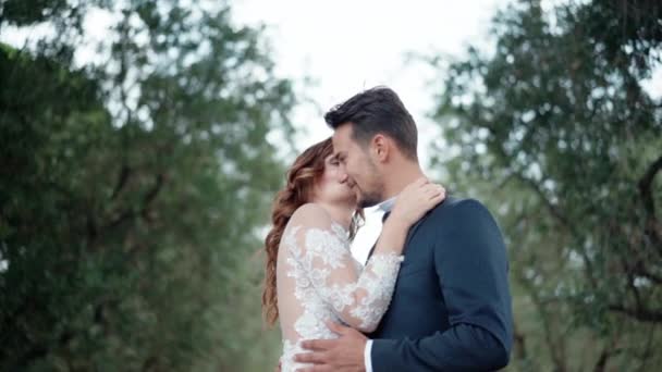 Emociones reales de la joven pareja casada feliz, recién casados abrazándose y mirándose a los ojos el uno al otro, pareja sonriente disfrutando el uno del otro en un hermoso jardín verde. Pasión y amor entre el hombre y la mujer — Vídeos de Stock