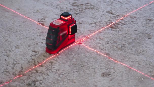 Красный лазерный прибор, установленный на полу на строительной площадке, строительный инструмент, измеряющий уровень грунта красным горизонтальным лазерным перекрестием. Рабочее оборудование, используемое в строительной промышленности и машиностроении — стоковое видео