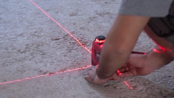 Operaio edile impostazione moderno livello laser sul pavimento sul cantiere per un'ulteriore misurazione, dispositivo di costruzione che mostra raggi rossi traversa per prendere misure accurate. Costruzione — Video Stock