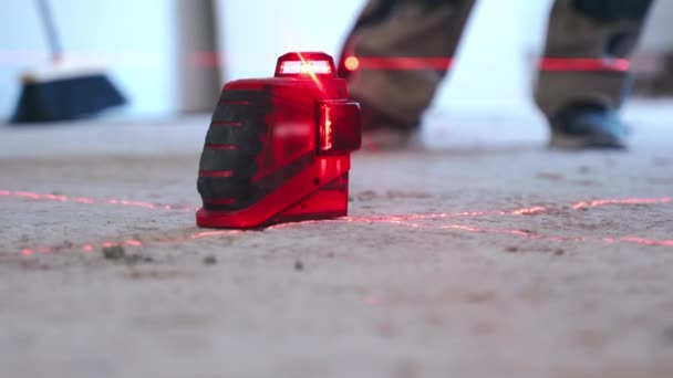 Stavební laserová úroveň instalovaná na podlaze na staveništi, červené laserové paprsky vytvářející horizontální průřez pro přesná měření ve stavebnictví. Moderní měřicí zařízení používané v — Stock video