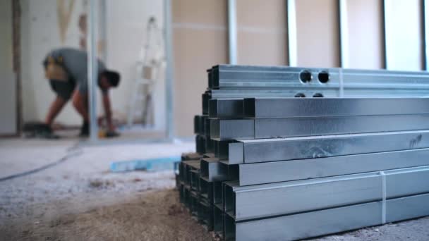 Stack of long metal construction profiles lying on blurred background of working engineer. Building worker measuring levels and distance, using electric screwdriver and drilling holes for drywalls — Stock Video