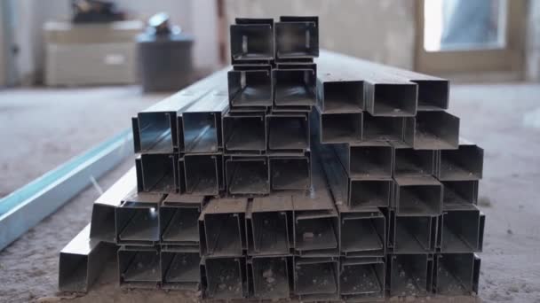 Stack of metal construction profiles on the ground in construction site. Necessary building materials for putting walls according to the house project. Steel panel installation indoors, house — Stock Video