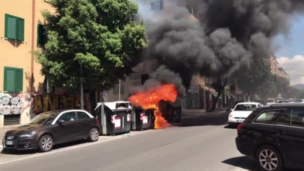 MILAN, ITALY - 12 ΙΟΥΝΙΟΥ 2020: Καίγοντας μαύρα πλαστικά δοχεία σκουπιδιών στο δρόμο στο Μιλάνο, πυροσβέστες σβήνουν φλόγες και βγαίνει μαύρος καπνός κοντά στα οικιστικά κτίρια. Σκόπιμος εμπρησμός — Αρχείο Βίντεο