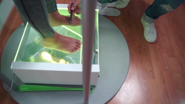 Primer plano de los pies de las pacientes femeninas en la superficie de vidrio transparente con luz de neón verde, mientras que el ortopedista masculino examinar y comprobar las condiciones de los pies y los huesos. Problemas con el pie plano y la salud — Vídeo de stock