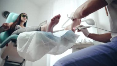 Ortopedi uzmanı üniformalı ve sağlık merkezinde çalışan koruyucu eldivenli bir doktor. Ayak tedavisi için lazer teknolojisi kullanan ayak doktoru. Tıbbi koltukta oturan kadın hasta...