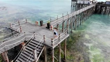 Genç çiftin ahşap köprüde sarılıp, öpüşüp, dans ederek yeşil yosunların arasında sığ bir yerde durduğunu gösteren hava manzarası. İnsanlar balaylarını Hint Okyanusu sahillerinde, yaz tatillerinde geçiriyorlar.