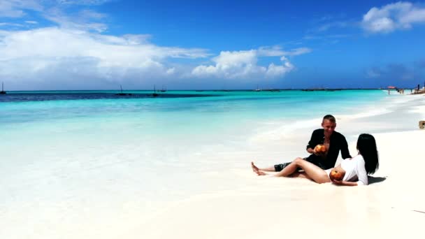 Красивая влюбленная пара, лежащая на удивительном белом песчаном пляже в окружении кристально чистой голубой воды океана. Туристы дегустируют экзотические фрукты и напитки на пляже, расслабляются во время летних каникул — стоковое видео
