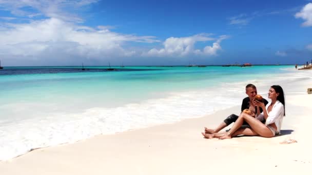 Niezapomniany miesiąc miodowy zakochanej młodej pary, ładna żona w białym bikini siedząca na białym piasku i degustująca egzotyczne napoje. Letni relaks w kurorcie Malediwy, para ciesząca się wakacjami — Wideo stockowe