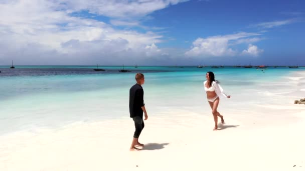 Casal feliz dançando na praia, movimentos de corpos sensíveis românticos de duas pessoas apaixonadas. Férias de verão de dois parceiros em local tropical exótico, água azul-turquesa incrível e pequenos barcos à vela — Vídeo de Stock