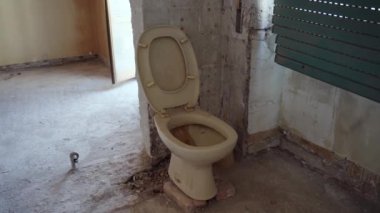 Terk edilmiş evdeki eski paslı, sarı tuvalet, soyulmuş duvara dayanmış seramik tıkanmış. Yıkık banyosu ve pis hijyenik olmayan tuvaleti olan bir evin içi. Onarılıyor