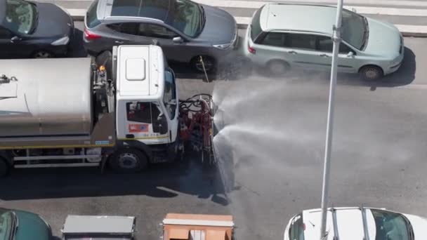 ROMA, ITALIA - 3 DE JULIO DE 2020: Vista superior del camión de barrido que pasa por la carretera y pulveriza agua bajo presión con aspersores especiales. Máquina de limpieza de calles, barredora pública de lavado de carreteras — Vídeos de Stock