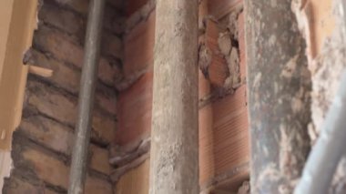 İnşaat alanındaki tuğla duvar boyunca uzanan eski dikey paslı borular çatlak boruları yıkmak ve yeni bakır boru hattının kurulumuna hazırlık yapıyor. Evde tamirat ve inşaat işleri var.