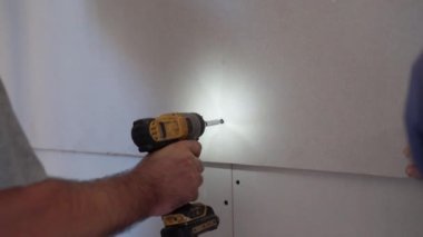 İnşaat işçileri inşaat alanına yeni alçıpan döşüyorlar, ustabaşı elektrikli tornavida kullanıyor ve daireye sondaj tahtası yerleştiriyor. Mühendislik endüstrisi ve takım çalışması kavramı