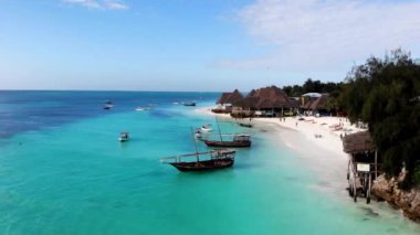 Küçük turistler ve balıkçı tekneleri Hint Okyanusu kıyısı boyunca turkuvaz su birikintisiyle yüzüyor. Deniz plajı boyunca yürüyen turistler, beyaz kum kıyısı boyunca yer alan ahşap evler. Yaz