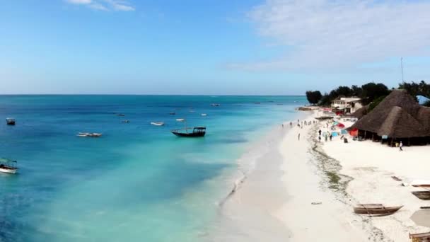 Famosas férias de verão resort, costa de areia branca cheia de turistas ambulantes. Vista aérea de água azul-turquesa com lotes de barcos à vela. Zanzibar mar praia resort — Vídeo de Stock