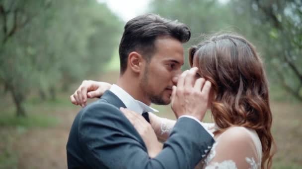 Jovens casais apaixonados abraçando, abraçando e beijando uns aos outros mostrando suas verdadeiras emoções encantadoras, apenas homens e mulheres casados desfrutando da presença uns dos outros no incrível jardim da oliveira. Casado — Vídeo de Stock