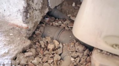 İnşaat alanındaki paslı tuvaletin altındaki gizli plastik kanalizasyon borusuna yakın çekim. Terk edilmiş evdeki tamirattan sonra yığınla konstrüksiyon israfı. Kanalizasyon sistemi ve su