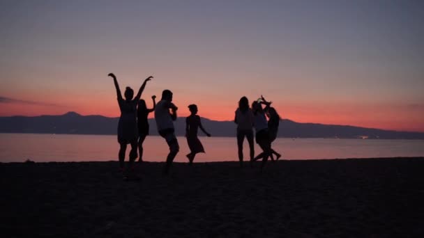 Güzel deniz günbatımı arka planında dans eden neşeli insanların siluetleri. Dans eden ve zıplayan arkadaşlar, plaj partisi ve disko müziği. Rahatlamak ve tatil yapmak için taze yaz içecekleri. — Stok video