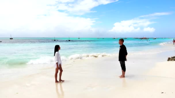 Casal romântico caminhando lentamente ao longo da praia de areia branca e abraçando, emoções sensíveis entre os amantes, menina bonita em biquíni branco se aproximando de seu namorado adorável e abraçando-o. Amor e — Vídeo de Stock