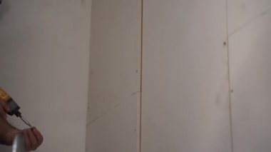 Elektrikli yelkovan tutan işçilerin yakın çekimleri ve daha fazla kalıp için alçıtaşı alçıpan delme delikleri. Müteahhit, moden daire tadilatı, alçı levhalar montajı