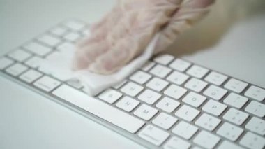 Beyaz koruyucu eldivenli adam ıslak antibakteriyel mendil kullanıyor ve klavye yüzeyinden kirli mikrop ve bakterileri çıkarıyor. Covid-19 salgını sırasında temizlik süreci ve önlem tedbirleri