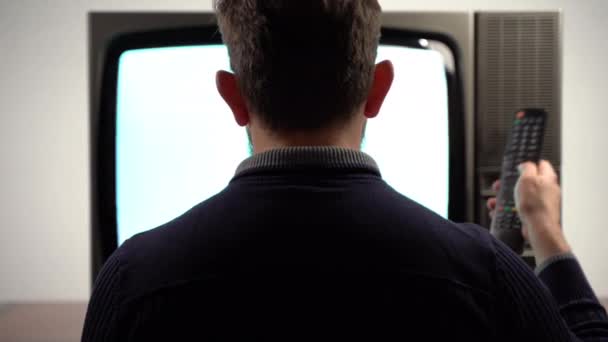 Back view of man holding retro TV remote control and changing media broadcast channels. Vintage broken television with blinking noise interference lines on screen. Media transmissions on retro TV — Stock Video