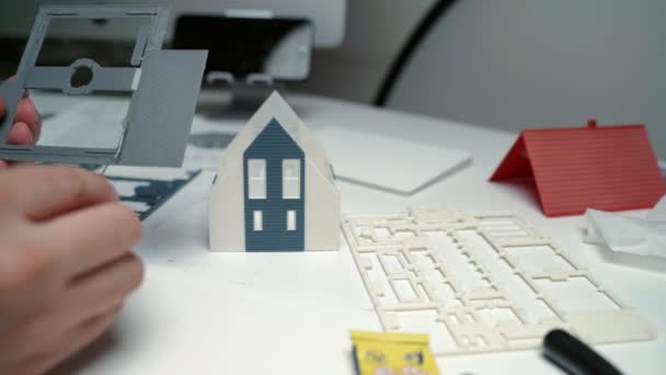 Architekt tworzący makietę domu mieszkalnego w miejscu pracy, projektant klejący plastikowe fundamenty konstrukcją ścian, miniaturowy dom dla klientów. Mały wirtualny dom z kolorowego plastiku — Wideo stockowe