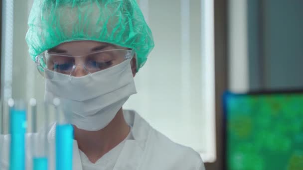 Female laboratory researcher in protective suit conducting scientific experiments using blue reagent, chemical elements and set of medical instruments. Chemist searching the way to create potential — Stock Video