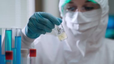 Koruyucu kaplamalı laboratuvar araştırmacısı sıvı çözeltisiyle tıbbi ampul sallıyor. Koronavirüs enfeksiyonuna karşı aşı geliştiren konsantre bir kimyager.