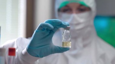 Açık sarı solüsyonlu steril tüpün yakın plan görüntüsü bulanık arkaplanda bilimsel araştırmacıların elinde. Korumacı kimyager covid-19 'a karşı potansiyel bir aşı ambolisi taşıyor.