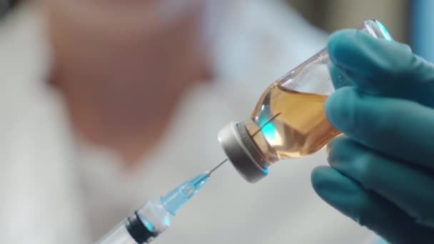 Detailní záběr potenciální vakcíny proti koronaviru nasáklé sterilní injekční jehlou, lékař v ochranných rukavicích natahuje lékařský roztok do injekční stříkačky. Vakcinační studie, laboratorní výzkum, kovid — Stock video