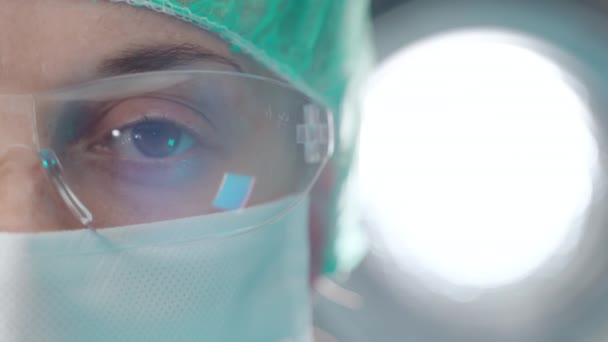 Vermoeide ogen van een zelfverzekerde dokter die op camera kijkt op een heldere achtergrond in het lab. Close-up gezicht van de vrouw in medische bril en masker, werken in het ziekenhuis tijdens coronavirus pandemie en — Stockvideo