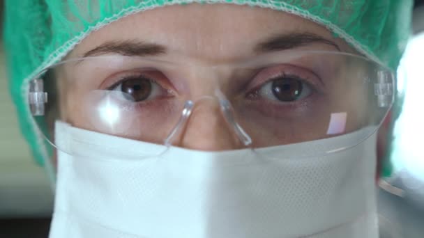 Retrato de cerca de los médicos ojos cansados con gafas protectoras y máscara médica. Especialista femenina de confianza mirando a la cámara después de un duro día de trabajo en el laboratorio de investigación. Experimentos médicos — Vídeo de stock