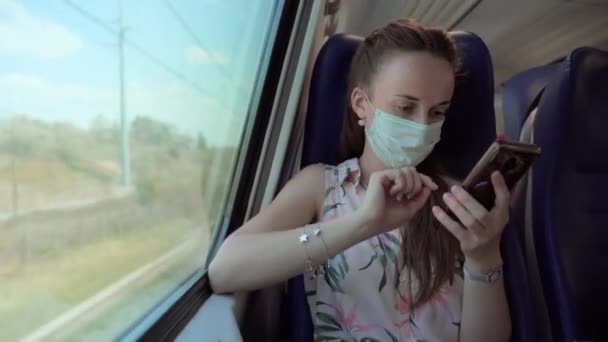 Tıbbi maskeli bir kadın trenle ve karanlık tünelden geçerken internetten sohbet etmek ve internette gezinmek için cep telefonu kullanıyor. Coronavirus sırasındaki toplu taşıma davranışları — Stok video