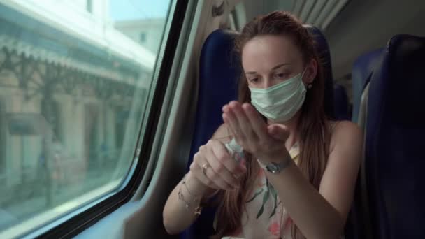 Soustředěná žena v lékařské masce pomocí dezinfekčního dávkovače s antibakteriálním gelem a pečlivě čistí ruce ve vlaku od bakterií, bakterií a mikrobů. Hygiena opatření na veřejných místech pro — Stock video