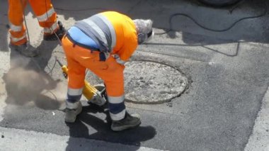 Koruyucu üniformalı yol işçileri elektrikli manuel makineyle beton kaldırım kırıyorlar veya daha fazla tadilat için çekiçle inşaat sahasında çalışıyorlar ve yol betonunu kesiyorlar. Mühendislik