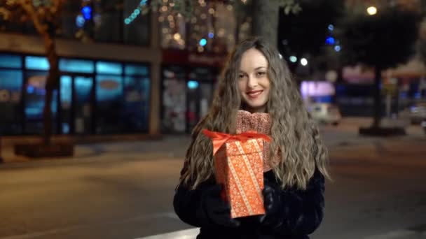Όμορφη γυναίκα με μακριά σγουρά μαλλιά και κόκκινα χείλη κρατώντας χριστουγεννιάτικο δώρο κουτί στα χέρια, χαμογελώντας και κοιτάζοντας την κάμερα. Όμορφη γυναίκα λαμβάνει ειδικά Χριστούγεννα δώρο και δείχνει την ευτυχία, γυναίκα σε — Αρχείο Βίντεο