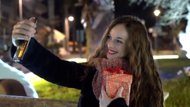 Bella donna con Natale presente in mano utilizzando smartphone e scattare foto selfie nel parco di notte, incredibile strada illuminata con luci di Natale e ghirlande, vacanze e Natale — Video Stock