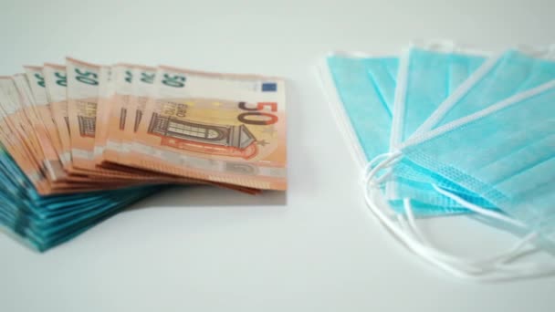 Una pila di banconote da 20 e 50 euro e due diversi tipi di maschere mediche protettive poste su sfondo bianco, che aumentano i prezzi dei medicinali e delle cure. Medicina costosa in periodo di mondo — Video Stock