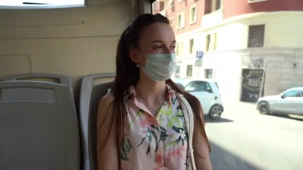 Mujer joven y cansada en máscara de protección médica conduciendo en transporte público a lo largo de las calles de la ciudad, mujer con ojos tristes siguiendo las medidas de precaución fuera y en transporte público. Urbano vacío — Vídeos de Stock