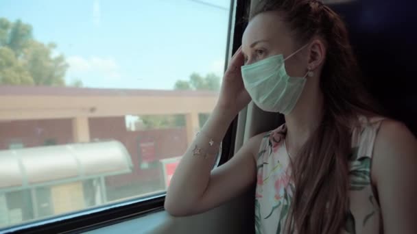 Smutná žena s zamyšlenýma očima, která měla na sobě lékařskou masku při jízdě vlakem, samice se chránila během pandemie koronaviru. Zákaz volného pohybu a koncepce sociální vzdálenosti — Stock video