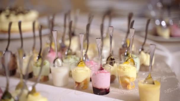 Pięknie urządzony stół bankietowy cateringowy z małymi szklanymi kieliszkami pełnymi galaretek, lodów i kawałków różnych owoców. Kolorowe kieliszki deserowe z łyżeczkami wewnątrz na blacie bufetowym — Wideo stockowe