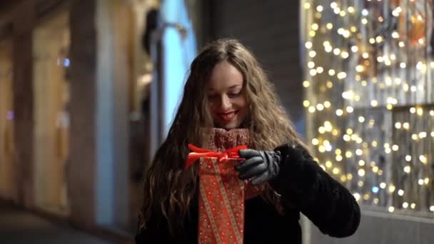 Retrato de la mujer joven increíble en brillantes luces de Navidad fondo apertura especial muy esperado regalo de Navidad y sonriente, feliz ffjalá mostrando sus verdaderas emociones sinceras después de recibir la Navidad — Vídeo de stock