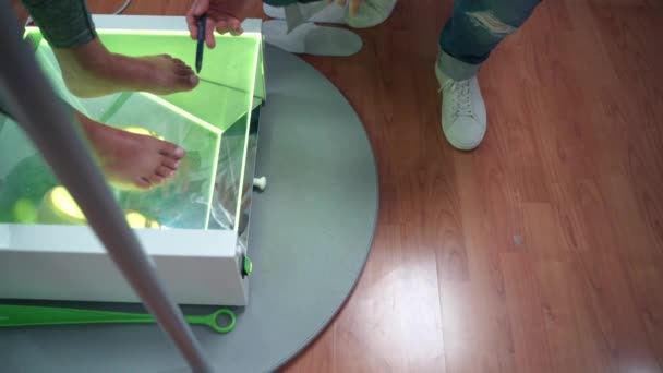 在骨科医生检查脚和骨状况时，赤脚女病人用绿色霓虹灯呆在透明的玻璃表面。医生解释扁足和足底的问题 — 图库视频影像