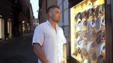 Moda butiğinin önünde ışıltılı dükkan vitrininde bir dizi kravat koleksiyonu sergilenen sıradan yaz kıyafeti giymiş bir adam. Erkek Shopofolik ilgi çekici kravatları izliyor, yakışıklı.