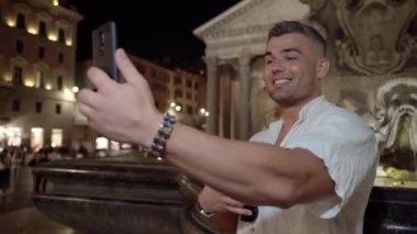 Kendine güvenen video içeriği yaratıcısı akıllı telefon kamerasıyla çevrimiçi dinleyicilerle video kaydı yapıyor, insanlarla konuşuyor ve onları motive ediyor. Çevrimiçi ders veren gülümseyen genç adam